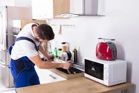 Technician working on a kitchen cooktop beside a microwave