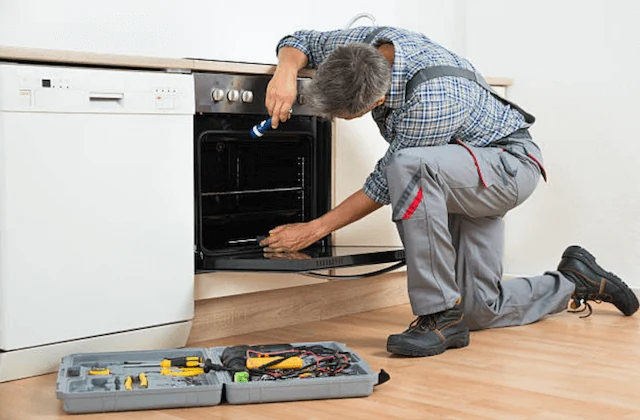 Technician using a flashlight to inspect an open oven